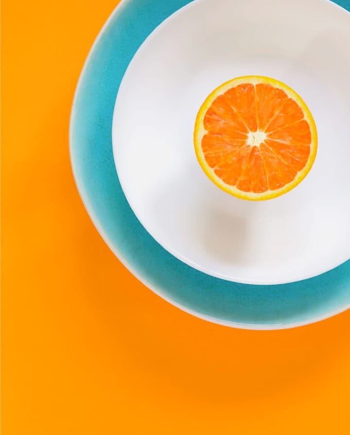 picture of a sliced orange on a white plate on a orang color background