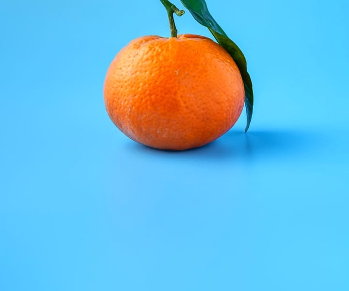 Pictures of a orange fruit with its leaf attached on a light blue background